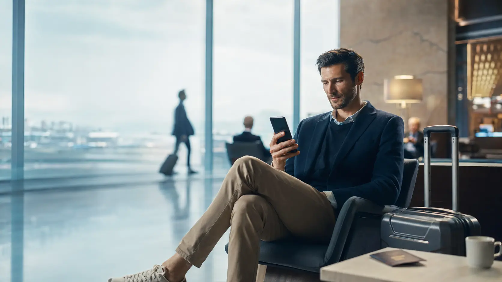 A traveller checking a phone in an airport lounge next to rolling luggage